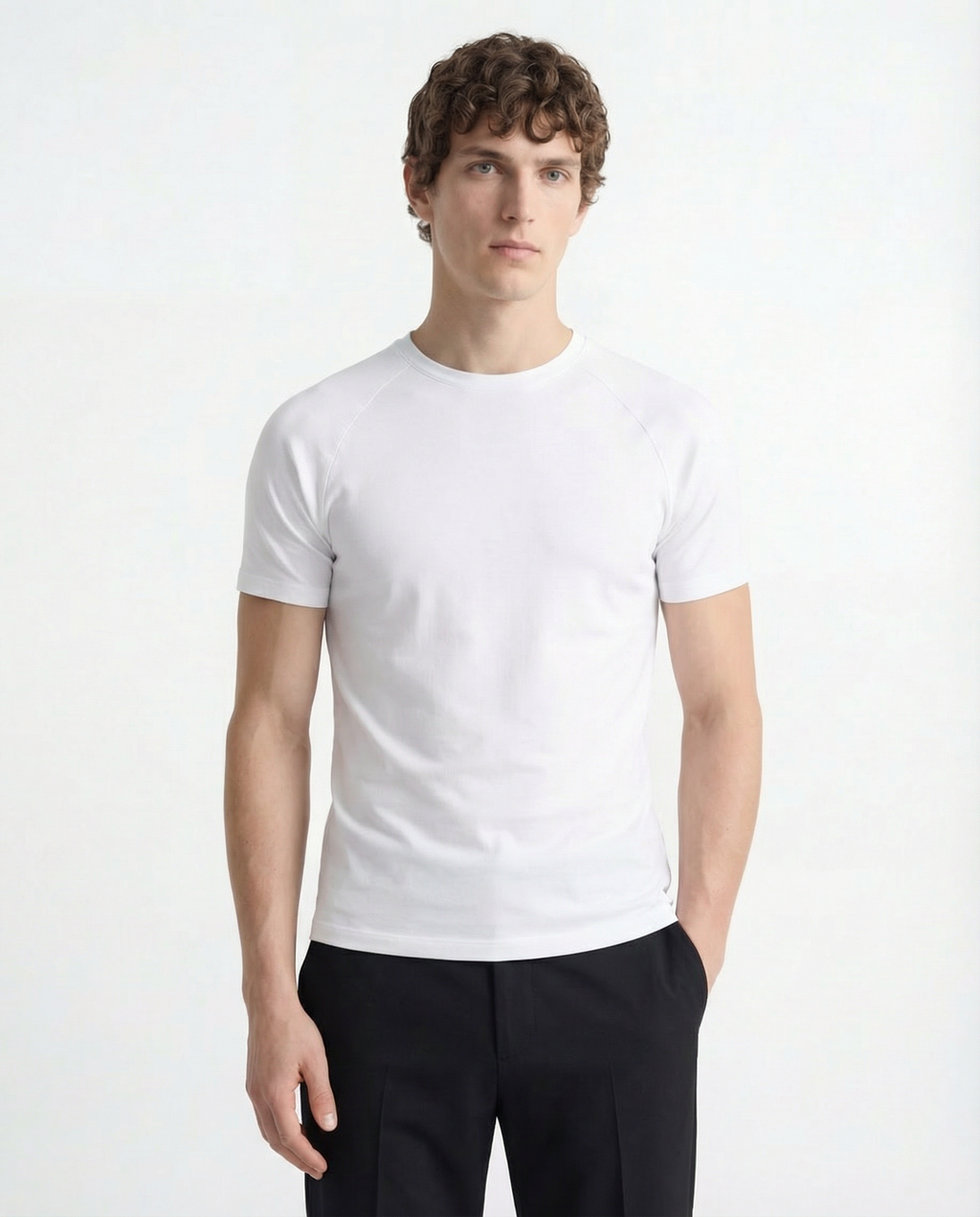 Man wearing a plain white t-shirt and black pants on a light gray background